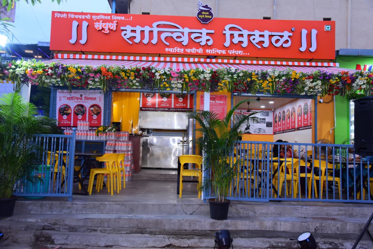 Daytime view of a Sampurn Satvik Misal outlet with flower decorations and outdoor seating